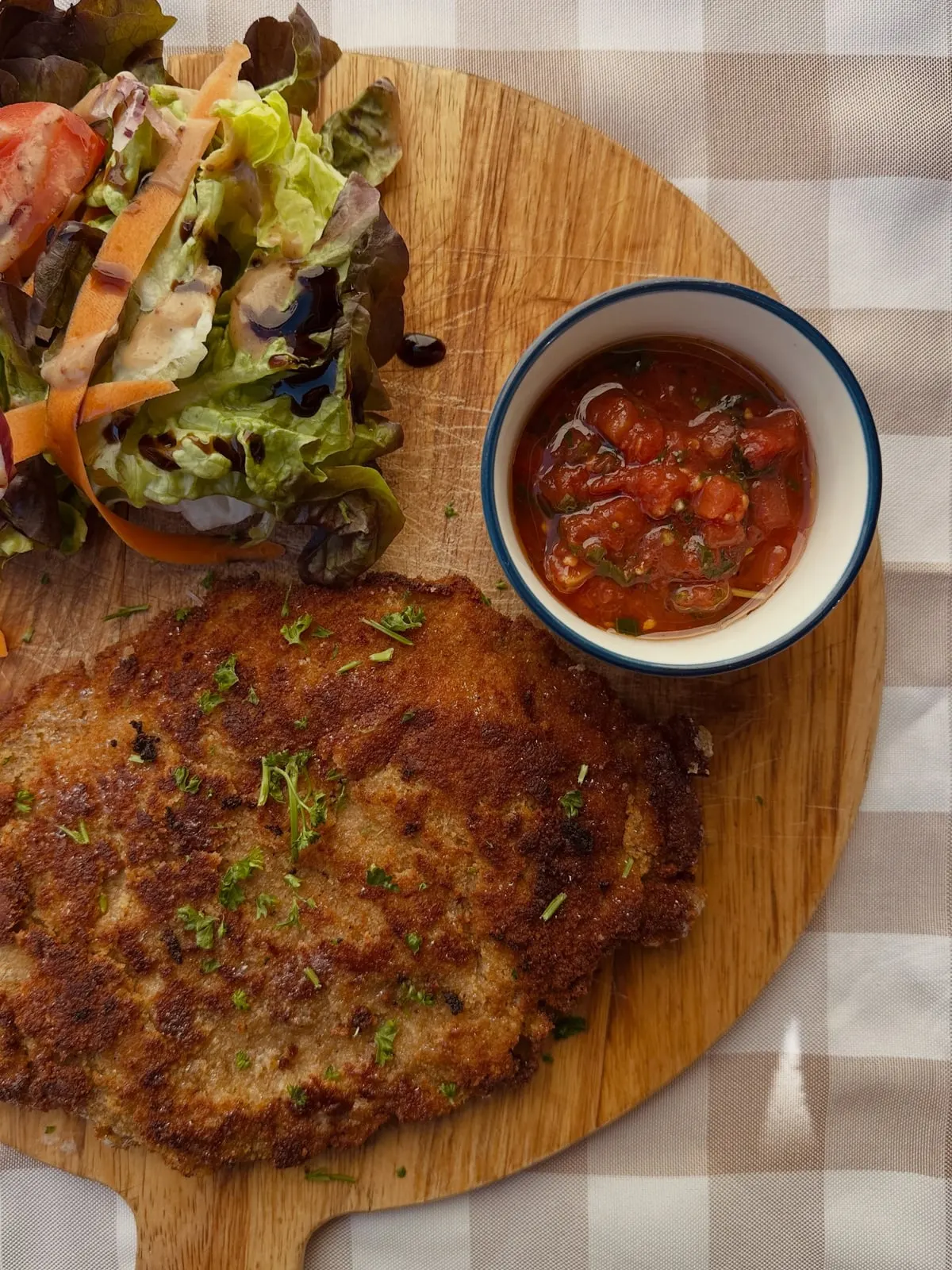 Escalope milanaise panée et salade servies sur planche en bois, nappe à carreaux, aux Cocottes