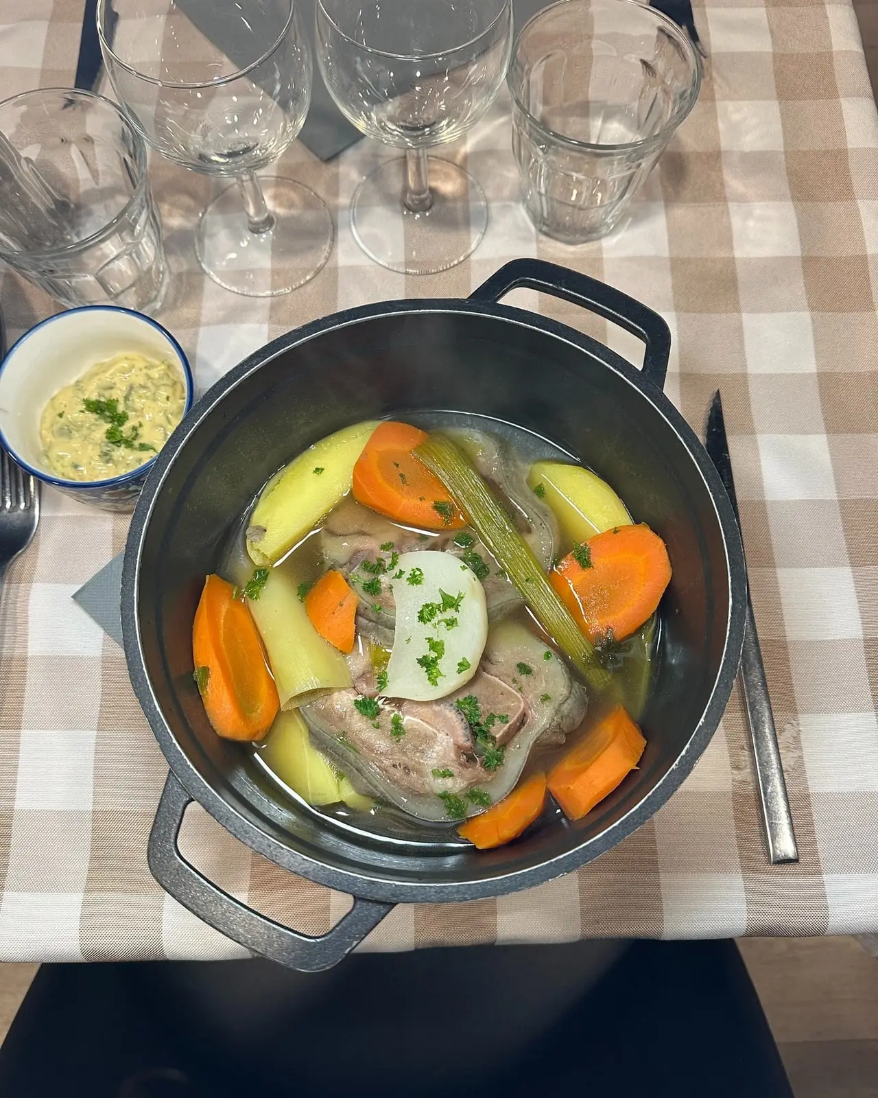 Plat mijoté aux légumes servi en cocotte en fonte sur nappe à carreaux au restaurant Les Cocottes